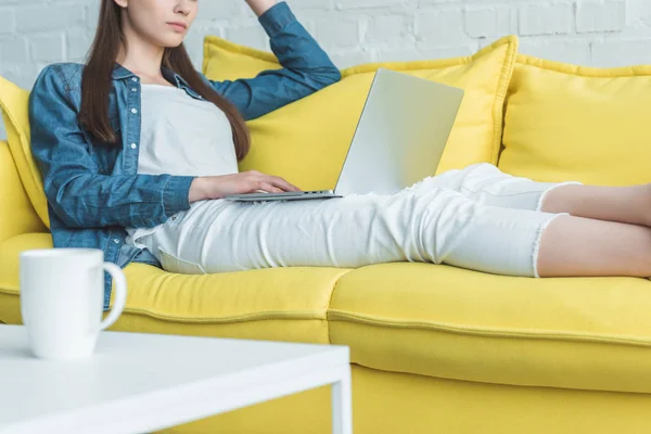 Cropped shot of girl sitting on sofa and using laptop at home — Stock Photo