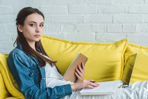 Girl looking at camera while studying with notebook and laptop at home — Stock Photo