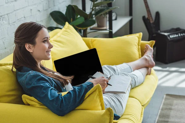 Schöne lächelnde Mädchen mit Laptop mit leerem Bildschirm und Notizen zu Hause — Stockfoto