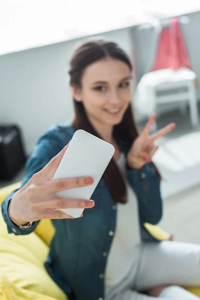 Foco seletivo de menina sorridente levando selfie com smartphone em casa — Fotografia de Stock