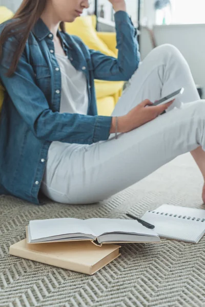 Cropped shot of girl using smartphone while studying at home — Stock Photo
