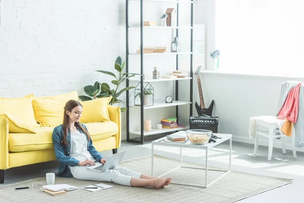 Vue grand angle de sourire jeune femme en utilisant un ordinateur portable tout en étudiant à la maison — Photo de stock