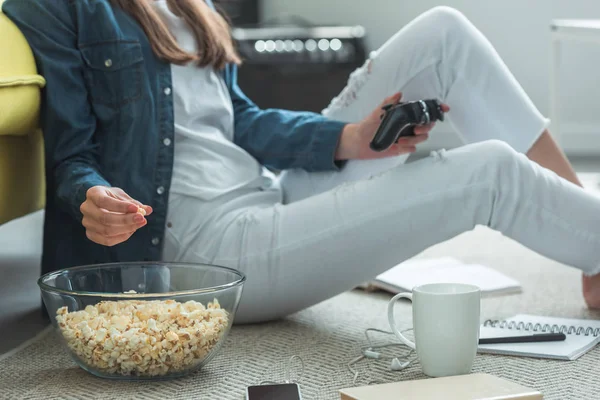 Tiro cortado de menina comendo pipoca e brincando com joystick em casa — Fotografia de Stock