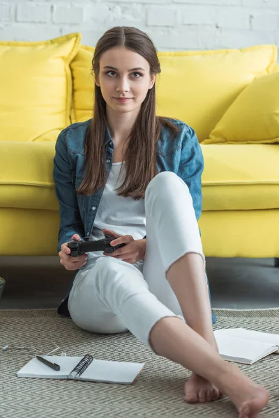 Hermosa adolescente sentada en la alfombra y jugando con joystick - foto de stock