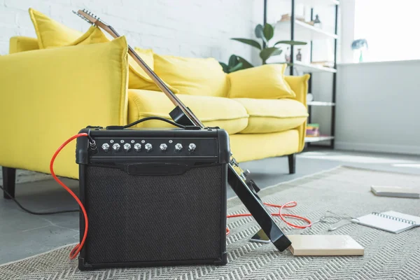 Guitare électrique et haut-parleur haut-parleur debout sur le sol avec des livres près du canapé — Photo de stock