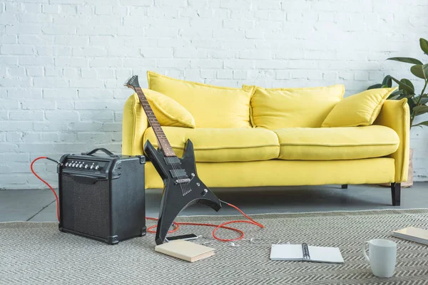 Guitare électrique, haut-parleur, smartphone, livres et tasse de café sur le sol près du canapé jaune dans le salon — Photo de stock