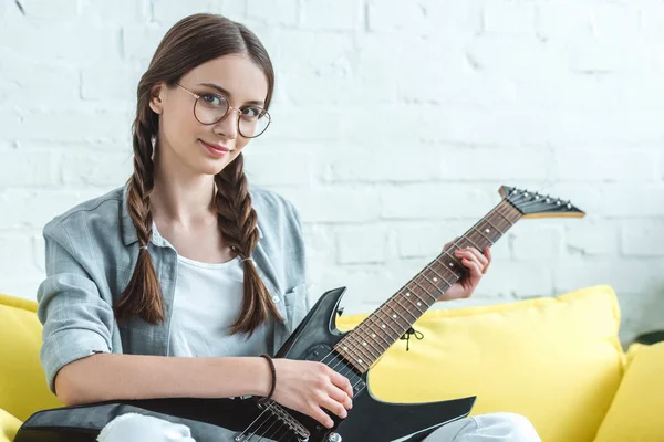 Atractiva adolescente femenina tocando la guitarra eléctrica en el sofá en casa - foto de stock