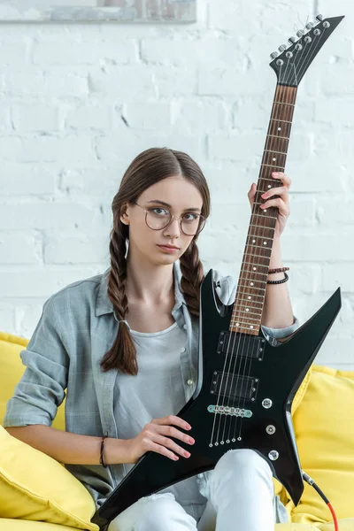 Atractiva chica adolescente sentada en el sofá con guitarra eléctrica - foto de stock