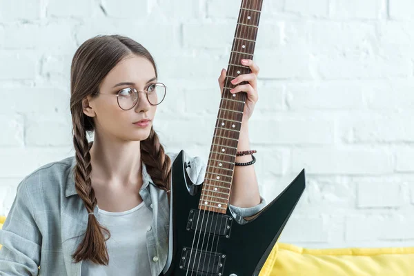 Hermosa chica adolescente sentada en el sofá con guitarra eléctrica - foto de stock