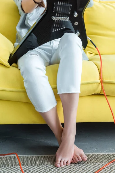 Cropped view of girl sitting on yellow sofa with electric guitar — Stock Photo