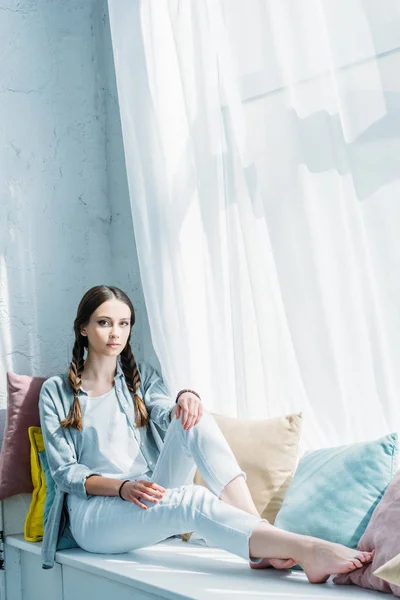 Belle adolescente assise sur le rebord de la fenêtre avec des oreillers — Photo de stock