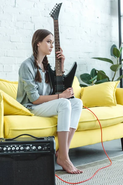 Teen girl sitting on sofa with electric guitar and loud speaker — Stock Photo