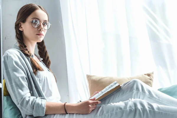 Menina bonita com tranças livro de leitura no peitoril da janela — Fotografia de Stock