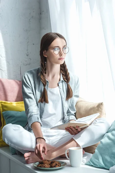 Beautiful girl reading book and eating cookies with coffee — Stock Photo