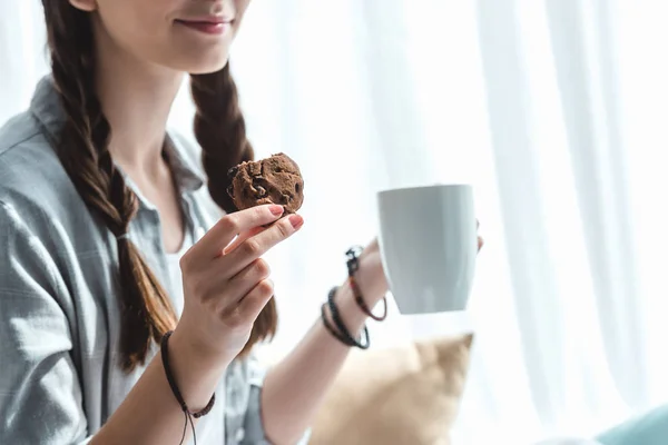 Cropped view of girl eating cookies with coffee — Stock Photo