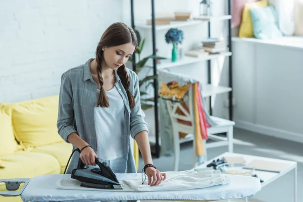 Schöne junge Frau bügelt weiße Hosen zu Hause — Stockfoto