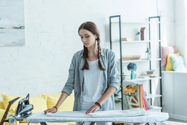 Adolescent fille avec fer et pantalon blanc sur planche à repasser — Photo de stock