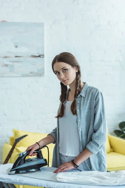 Atractiva chica adolescente planchando pantalones blancos en la sala de estar - foto de stock