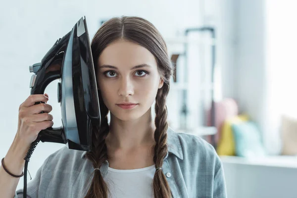 Hermosa chica con trenzas sosteniendo hierro cerca de la cabeza - foto de stock