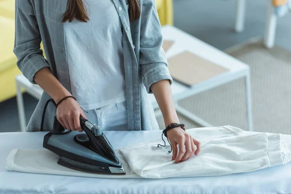 Abgeschnittene Ansicht eines Mädchens, das zu Hause weiße Hosen bügelt — Stockfoto