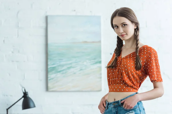 Schöne Teenie-Mädchen mit Zöpfen stehen im Zimmer mit Malerei an der Wand — Stockfoto