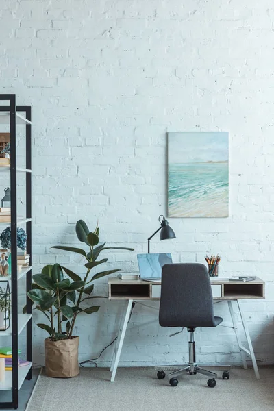 Estantería y mesa con portátil en la sala de estar con pintura en la pared — Stock Photo