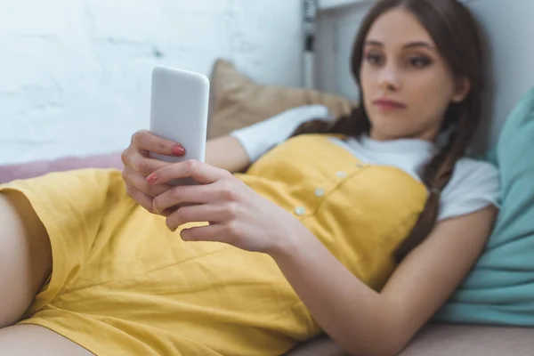 Selective focus of teen girl using smartphone and lying on sofa — Stock Photo
