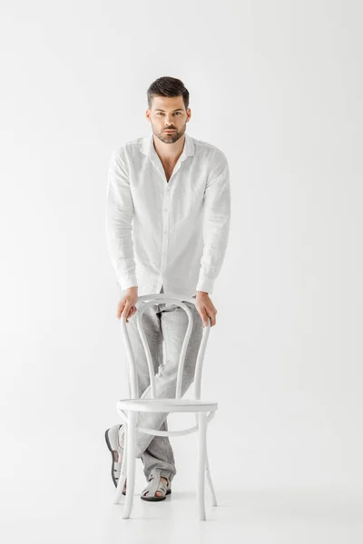 Junger Mann in Leinenkleidung steht in der Nähe von Stuhl isoliert auf grauem Hintergrund — Stockfoto