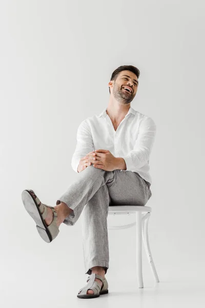 Hombre riendo en ropa de lino sentado en silla aislado sobre fondo gris - foto de stock