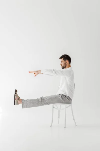 Perfil do modelo masculino em roupas de linho sentado na cadeira com as pernas esticadas e as mãos isoladas em fundo cinza — Fotografia de Stock