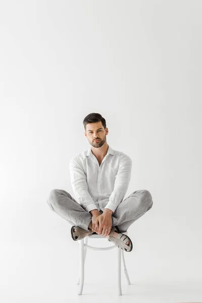 Hombre serio en ropa de lino sentado en silla aislado sobre fondo gris - foto de stock