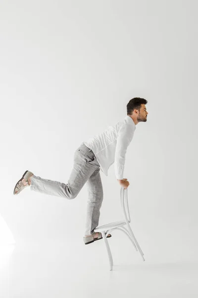 Вид сбоку человека в льняной одежде, балансирующего на стуле, изолированном на сером фоне — стоковое фото