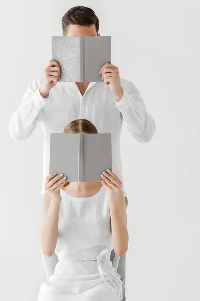 Paar in Leinenkleidern verdeckt Gesichter durch Bücher auf grauem Hintergrund — Stockfoto