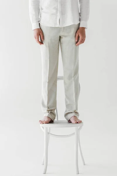 Imagen recortada del hombre en ropa de lino de pie en silla aislada sobre fondo gris - foto de stock