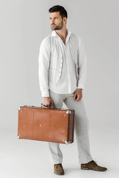 Serious stylish male traveler in linen clothes holding vintage suitcase isolated on grey background — Stock Photo