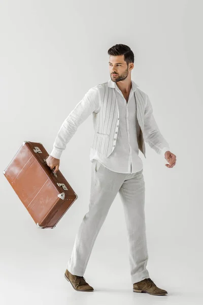 Stylish male tourist in linen clothes carrying vintage suitcase isolated on grey background — Stock Photo