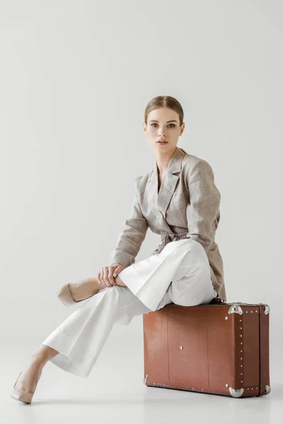 Jeune touriste féminine élégante assise sur une valise vintage isolée sur fond gris — Photo de stock