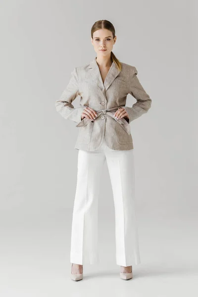 Beautiful stylish woman adjusting belt of linen jacket isolated on grey background — Stock Photo