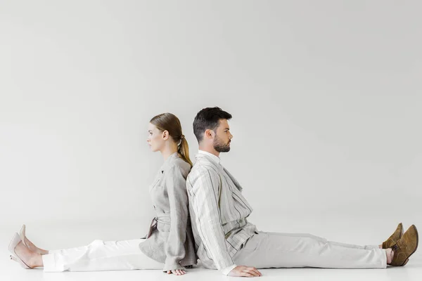 Couple of models in vintage clothes sitting on floor and leaning back to back on white — Stock Photo