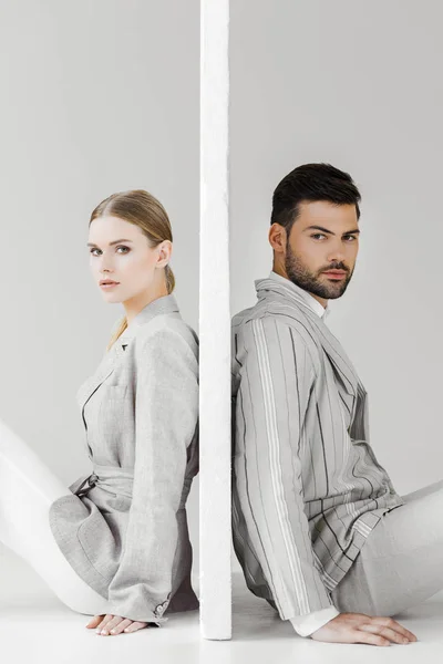 Side view of couple of models in stylish jackets leaning back on sides of wall on white and looking at camera — Stock Photo