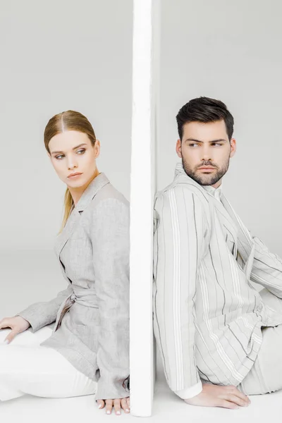 Side view of couple of models in stylish jackets leaning back on sides of wall on white and looking at each other — Stock Photo