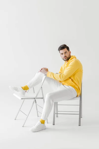 Attractive young man in yellow hoodie sitting on chairs on white — Stock Photo