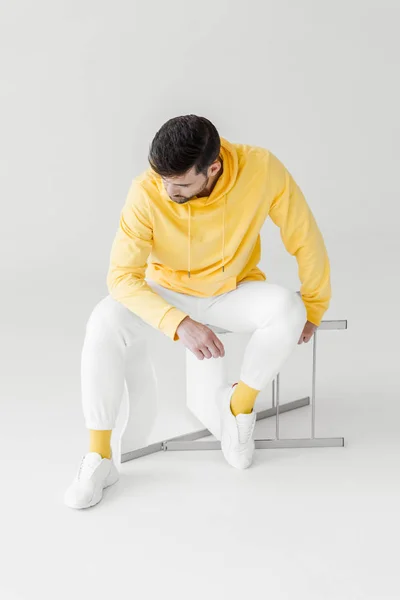 Thoughtful young man in yellow hoodie sitting on flipped chair on white — Stock Photo