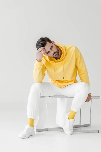 Stylish young man in yellow hoodie sitting on flipped chair on white — Stock Photo