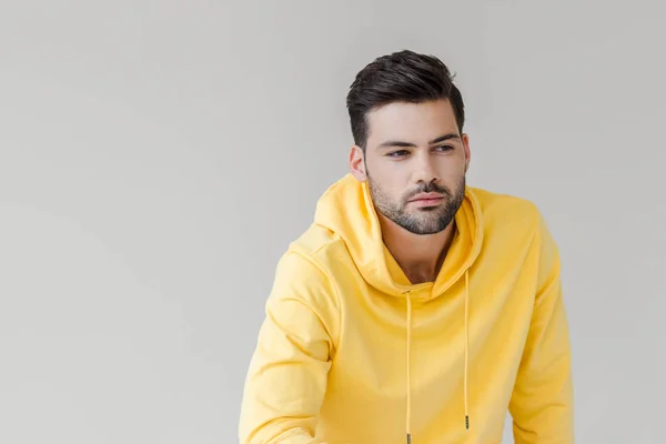 Schöner junger Mann in gelbem Kapuzenpulli, der isoliert auf weißem Grund wegschaut — Stockfoto