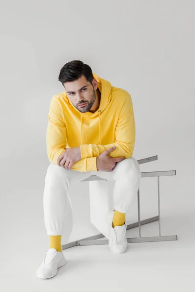 Joven guapo en sudadera con capucha amarilla sentado en silla volteada en blanco - foto de stock