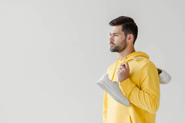 Beau jeune homme en sweat à capuche jaune avec des baskets blanches suspendues sur l'épaule isolé sur blanc — Photo de stock