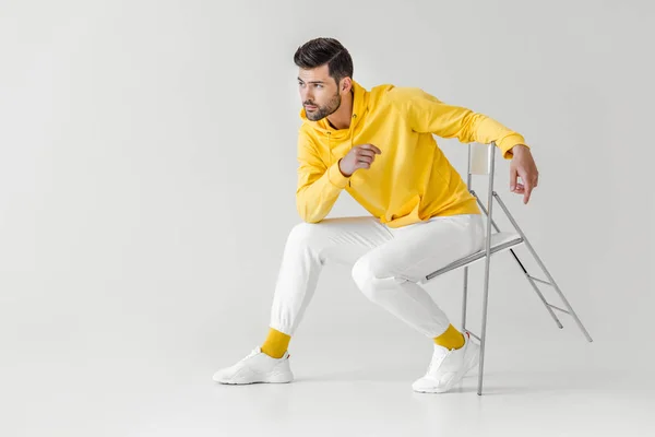 Elegante giovane uomo con cappuccio giallo seduto sulla sedia su bianco — Foto stock