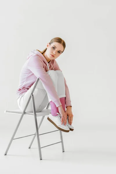 Привлекательная молодая женщина в розовой толстовке сидит на стуле на белом — стоковое фото