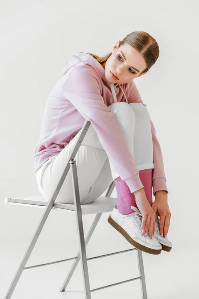 Élégant jeune femme en sweat à capuche rose assis sur la chaise sur blanc — Photo de stock